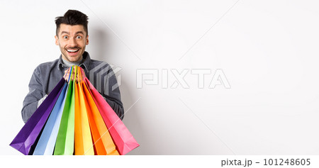 Excited smiling guy holding colorful shopping bags and rejoicing with discounts in store, standing against white background Excited smiling guy holding colorful shopping bags and rejoicing with discounts in store, standing against white background 101248605