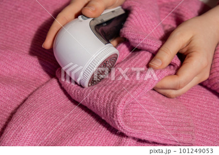 Woman using Anti-pilling razor at home. Device for shaving clothes. Anti-Plush fabric Shaver. Electric portable sweater pill defuzzer Lint remover from pink acrylic or wool sweater. Slow fashion Woman using Anti-pilling razor at home. Device for shaving clothes. Anti-Plush fabric Shaver. Electric portable sweater pill defuzzer Lint remover from pink acrylic or wool sweater. Slow fashion 101249053