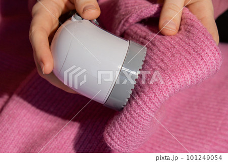 Woman using Anti-pilling razor at home. Device for shaving clothes. Anti-Plush fabric Shaver. Electric portable sweater pill defuzzer Lint remover from pink acrylic or wool sweater. Slow fashion Woman using Anti-pilling razor at home. Device for shaving clothes. Anti-Plush fabric Shaver. Electric portable sweater pill defuzzer Lint remover from pink acrylic or wool sweater. Slow fashion 101249054