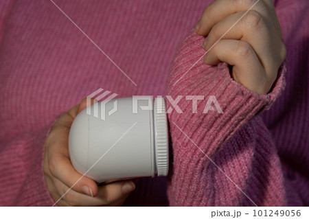 Woman using Anti-pilling razor at home. Device for shaving clothes. Anti-Plush fabric Shaver. Electric portable sweater pill defuzzer Lint remover from pink acrylic or wool sweater. Slow fashion Woman using Anti-pilling razor at home. Device for shaving clothes. Anti-Plush fabric Shaver. Electric portable sweater pill defuzzer Lint remover from pink acrylic or wool sweater. Slow fashion 101249056