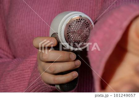 Woman using Anti-pilling razor at home. Device for shaving clothes. Anti-Plush fabric Shaver. Electric portable sweater pill defuzzer Lint remover from pink acrylic or wool sweater. Slow fashion 101249057