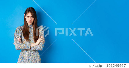 Angry young woman in dress feel unfair, cross arms on chest and frowning offended, standing on blue background 101249467