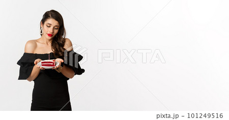 Party and celebration. Cute young woman with red lips, wearing black dress, holding birthday cake with candle and looking dreamy, making wish, white background 101249516