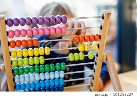 Little preschool girl playing with educational wooden rainbow toy counter abacus. Healthy happy child with glasses learning to count and colors, indoors on sunny day. 101253224