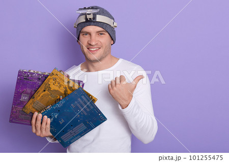 Happy smiling radiotrician wears casual outfit with magnifier on her forehead, holding three multicolored motherboards or flares in hand, showing something aside with his thumb. Electronic engineering Happy smiling radiotrician wears casual outfit with magnifier on her forehead, holding three multicolored motherboards or flares in hand, showing something aside with his thumb. Electronic engineering 101255475