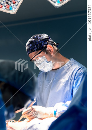 The doctor performs an operation in a dark operating room with a lamp in the background, a professional surgeon during a stressful operation. The doctor performs an operation in a dark operating room with a lamp in the background, a professional surgeon during a stressful operation. 101257324