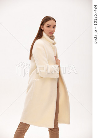 Fashionable self-confident girl in a light faux fur coat. Modern fashion trend for fur coats made of faux fur. Model posing in a fur coat on a light background 101257434