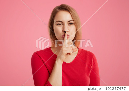 Portrait of secret beautiful young woman keeps fore finger on lips, shows silence sign, tries to keep personal information in secret, isolated over pink background. Hush or stop talking, please Portrait of secret beautiful young woman keeps fore finger on lips, shows silence sign, tries to keep personal information in secret, isolated over pink background. Hush or stop talking, please 101257477