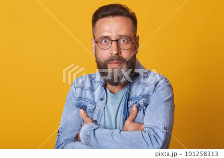 Portrait of shocked middle aged man in full disbelief. Hipster male with beard wears denim jacket posing isolated over yelow studio background. Astonished face expression, human emotion, body language 101258313