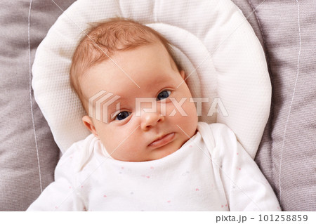 Charming adorable newborn child in a white shirt lies in a rocking chair looking at the camera, happy carefree childhood, exploring the world around her. 101258859
