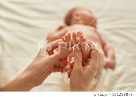 Faceless person making baby massage for infant lying on bed, mommy massaging new born baby with love, mum gently touching kid's feet for development of coordination of movements. Faceless person making baby massage for infant lying on bed, mommy massaging new born baby with love, mum gently touching kid's feet for development of coordination of movements. 101258878
