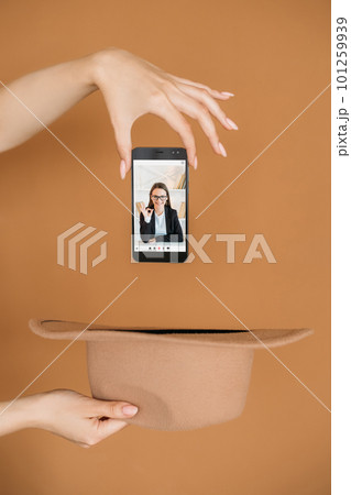 E-learning knowledge. Distance study. Video conference. Digital education. Female hand dropping phone with satisfied online teacher on screen into hat on brown. E-learning knowledge. Distance study. Video conference. Digital education. Female hand dropping phone with satisfied online teacher on screen into hat on brown. 101259939