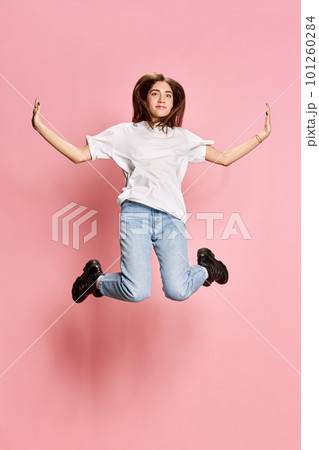 Full-length portrait of young, beautiful, brunette girl in casual clothes jumping against pink studio background. Relaxation 101260284