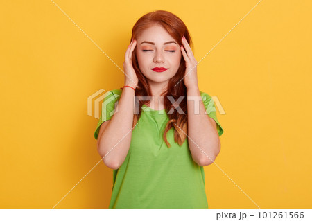 Portrait of charming, stylish woman in green shirt having head ache, touching temples with fingers and close eyes, standing over yellow background. Portrait of charming, stylish woman in green shirt having head ache, touching temples with fingers and close eyes, standing over yellow background. 101261566