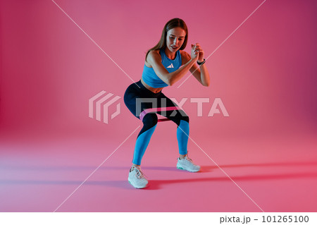 Strong woman in sportswear performs fitness exercises with resistance band on studio background Strong woman in sportswear performs fitness exercises with resistance band on studio background 101265100