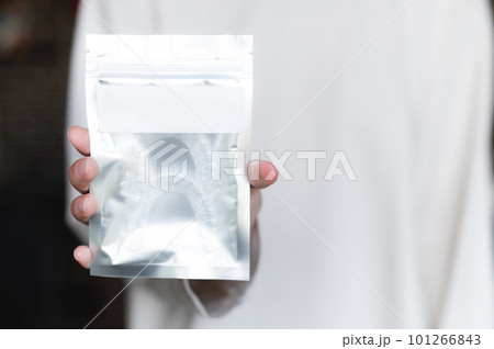 female hand hold a silver small package with an empty tag on the background of herself, a close-up of an object for advertising 101266843