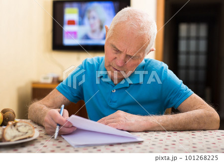 Serious older man writing letter at table in living room 101268225