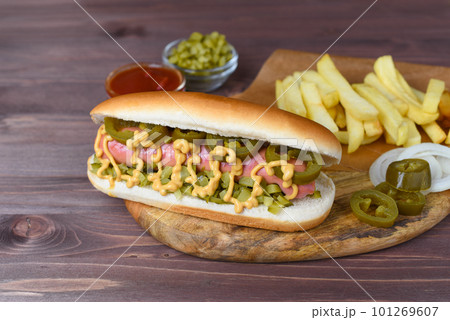 Homemade Hot Dog With Yellow Mustard, Ketchup, Onion, Pickles and French Fries. Ready-to-eat. Hotdog on rustic background. Sausage in bun with pickles. Homemade Hot Dog With Yellow Mustard, Ketchup, Onion, Pickles and French Fries. Ready-to-eat. Hotdog on rustic background. Sausage in bun with pickles. 101269607