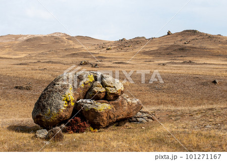 White bones lie between large boulders in the form of an altar in the steppe. Brown tones. Cloudy. The hills are behind. White bones lie between large boulders in the form of an altar in the steppe. Brown tones. Cloudy. The hills are behind. 101271167