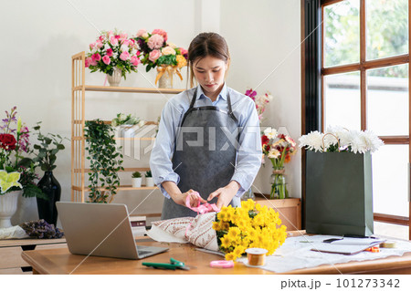 Female florist in apron using craft paper to wrapping yellow chr 101273342