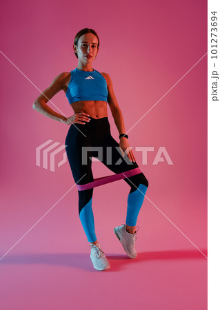 Athletic woman trains legs with fitness elastic band on studio background 101273694