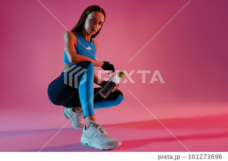Healthy woman sitting with water bottle in sport clothing over studio background Healthy woman sitting with water bottle in sport clothing over studio background 101273696