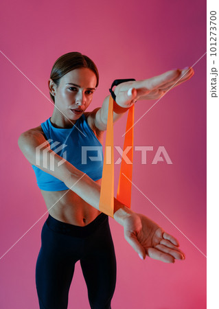 Sports woman with her hands stretches rubber elastic band for training on studio background 101273700