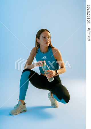 Active woman drinking water from bottle while workout and doing sport exercises on studio background 101273702