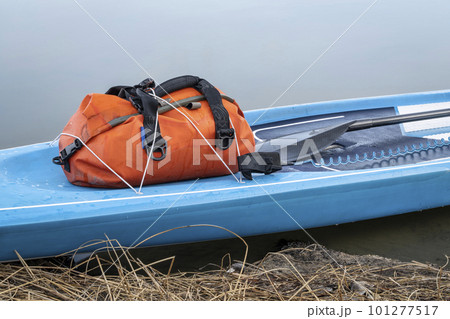 touring stand up paddleboard with a waterproof duffel, paddle and safety leash on a lake shore, early spring in Colorado touring stand up paddleboard with a waterproof duffel, paddle and safety leash on a lake shore, early spring in Colorado 101277517