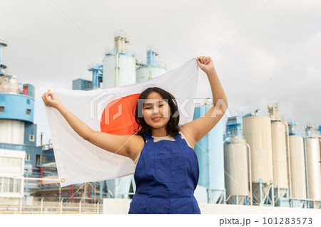 Happy young woman with flag of Japan against background of factory 101283573