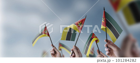 A group of people holding small flags of the Mozambique in their hands A group of people holding small flags of the Mozambique in their hands 101284282