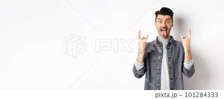 Excited funny guy showing tongue and heavy metal horns sign, enjoying party or event, having fun, standing on white background 101284333