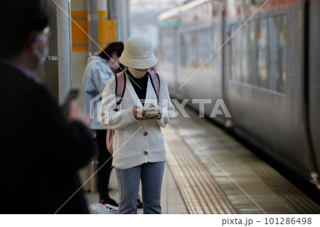 駅のホームで電車を待ちながらスマートフォンを弄る若い女性の姿 駅のホームで電車を待ちながらスマートフォンを弄る若い女性の姿 101286498