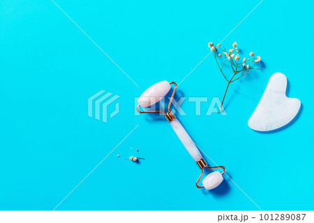 Rose quartz facial massage roller over blue background. Massage tools with jade stone, anti-wrinkle beauty skincare tool. View from above. Copy space. 101289087