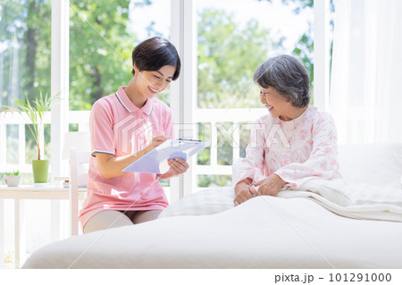 訪問介護　ベットに座るシニア女性から聞き取りをする介護士 101291000