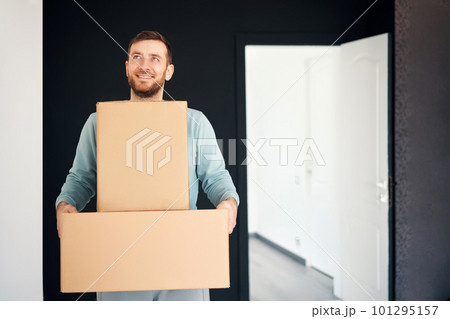 Young smiling man moving into new apartment carrying cardboard boxes 101295157