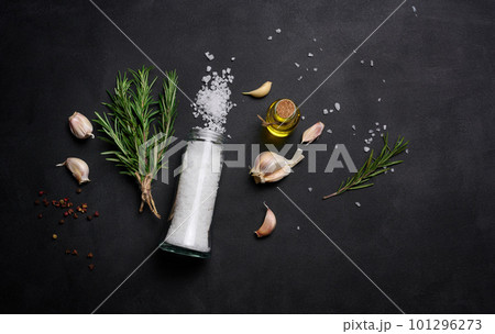 Scattered coarse white salt, peppercorns and rosemary sprigs on a black table, ingredients for cooking fish and meat Scattered coarse white salt, peppercorns and rosemary sprigs on a black table, ingredients for cooking fish and meat 101296273