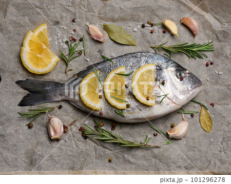 Raw whole dorado fish on brown parchment paper and spices for cooking, top view on black table Raw whole dorado fish on brown parchment paper and spices for cooking, top view on black table 101296278
