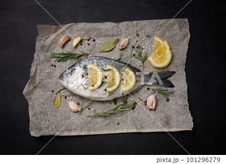 Raw whole dorado fish on brown parchment paper and spices for cooking, top view on black table Raw whole dorado fish on brown parchment paper and spices for cooking, top view on black table 101296279