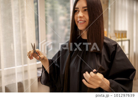 Smiling beautiful girl holds scissors and bun of her cut hair in her hands Smiling beautiful girl holds scissors and bun of her cut hair in her hands 101297639