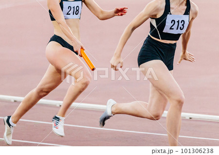 women running relay race in summer athletics championship, passing baton two female athletes women running relay race in summer athletics championship, passing baton two female athletes 101306238