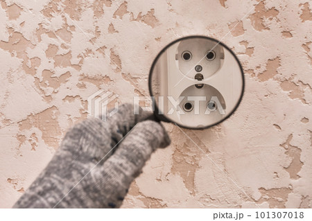 The hand of a construction worker in protective gloves examines through a magnifying glass the connection of appliances in the house 101307018