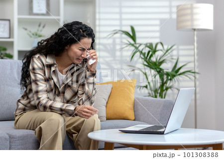 Online consultation with a psychologist, woman crying at home complaining to doctor on video call, Hispanic woman with curly hair talking to support service using laptop sitting on sofa at home. Online consultation with a psychologist, woman crying at home complaining to doctor on video call, Hispanic woman with curly hair talking to support service using laptop sitting on sofa at home. 101308388