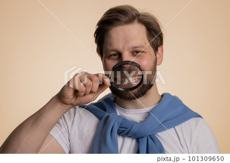Caucasian man holding magnifier glass on teeth, looking at camera showing funny smiling face mouth Caucasian man holding magnifier glass on teeth, looking at camera showing funny smiling face mouth 101309650