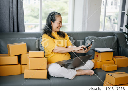 Startup small business SME, Entrepreneur owner Senior woman using smartphone or tablet taking receive and checking online purchase shopping order to preparing pack product box. 101313658