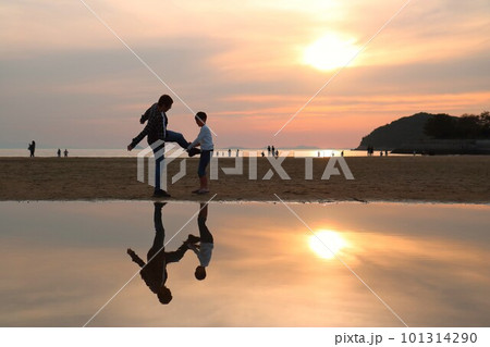 夕暮れの浜辺でキックのまねをする父親と息子 101314290