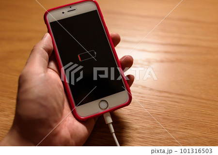バッテリー充電切れでケーブルで充電する使用感ある古いスマホを持つ男性　机の上に置かれたスマートフォン 101316503