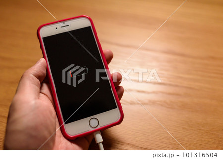 バッテリー充電切れでケーブルで充電する使用感ある古いスマホを持つ男性　机の上に置かれたスマートフォン 101316504