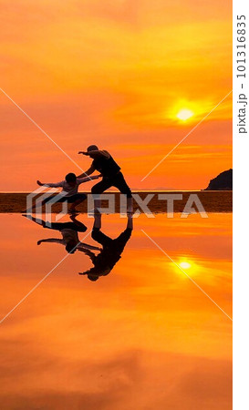 浜辺で夕日を背に格闘技のまねをする女性と少年のシルエット　 101316835
