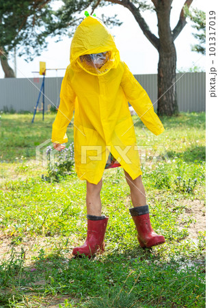 A girl in red rubber boots and a yellow raincoat runs through puddles after a rain in the village. Summer time, freedom, childhood A girl in red rubber boots and a yellow raincoat runs through puddles after a rain in the village. Summer time, freedom, childhood 101317019